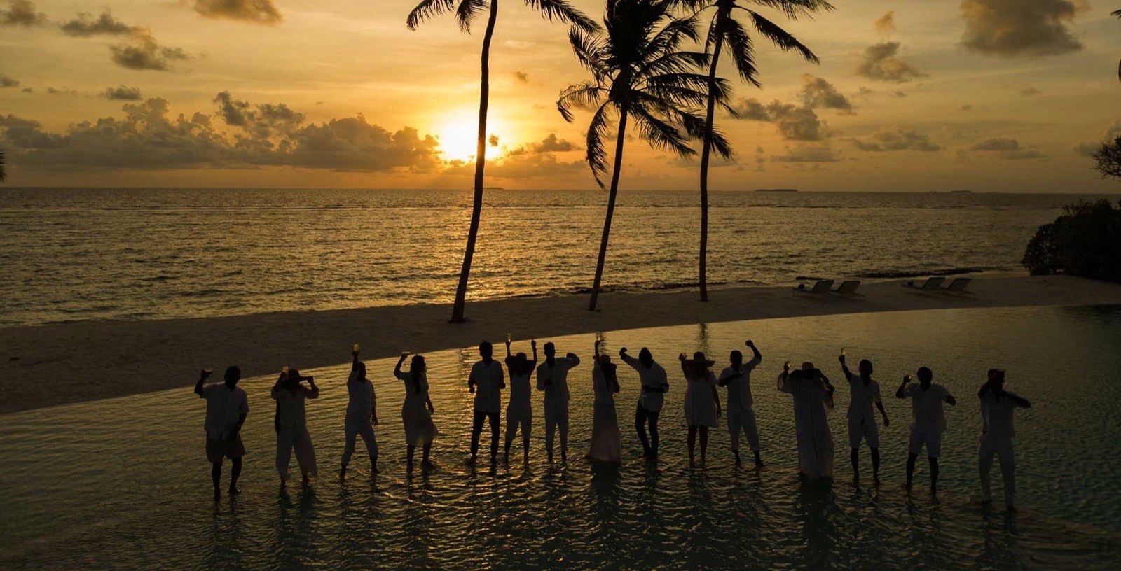 A sunset gathering by the pool, guests in white with the sky turning gold.